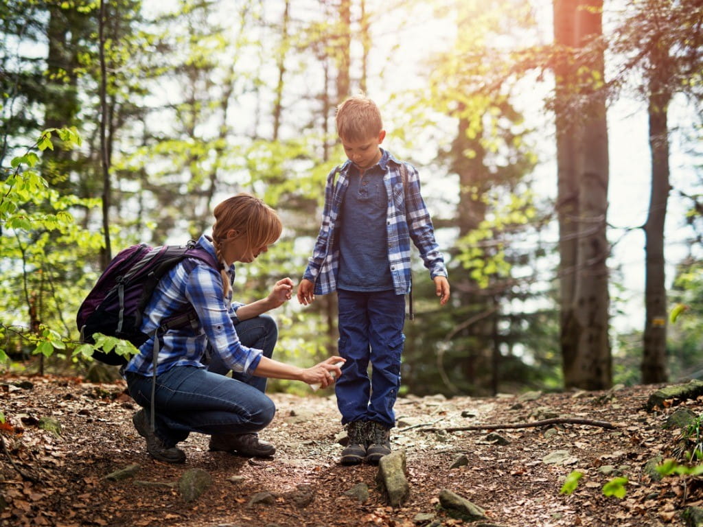 mother applying tick repellent on son in the woods