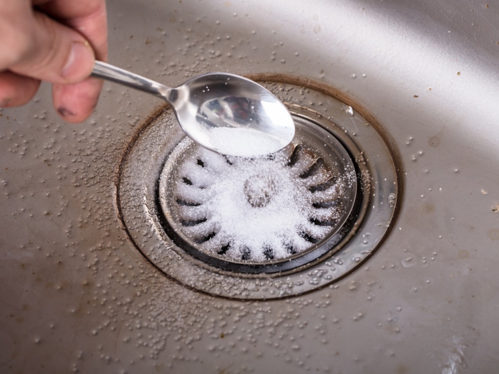 person using baking soda to clean drain